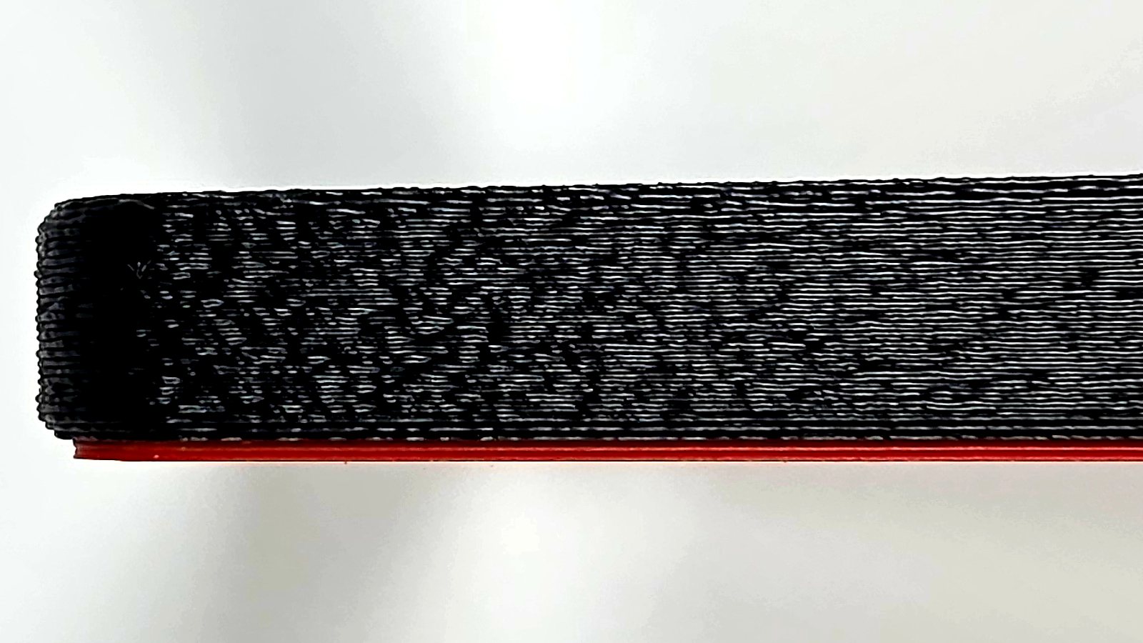 The side of the black printed bumper edge on, showing the fine fuzzy-skin texture with a thin scarlet red line beneath